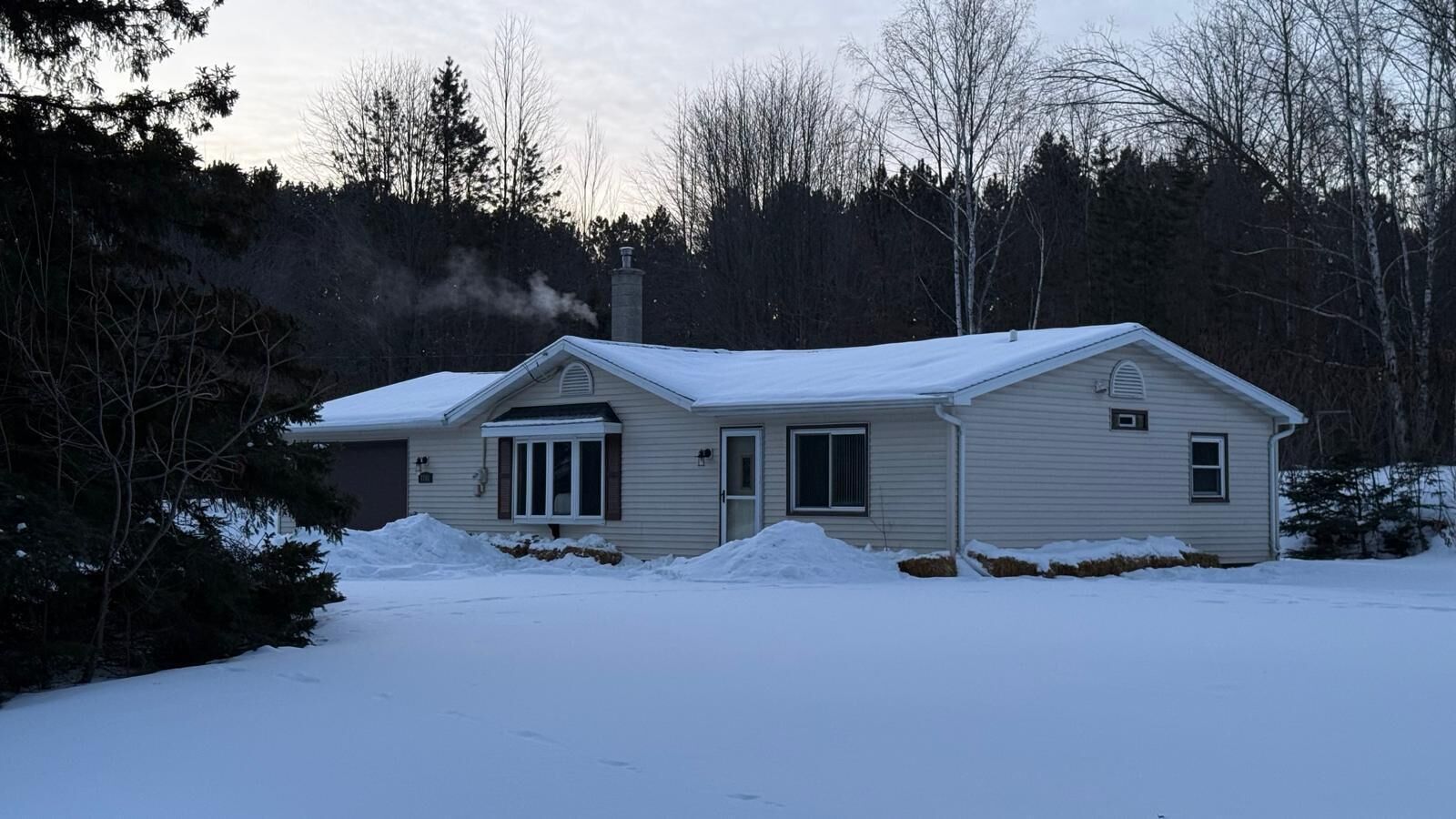 A single-story house with a snow-covered roof and a chimney emitting smoke.