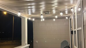 Ett takförsett utomhusområde med ett bord och stolar, ljusslingor och utsikt över gatan.