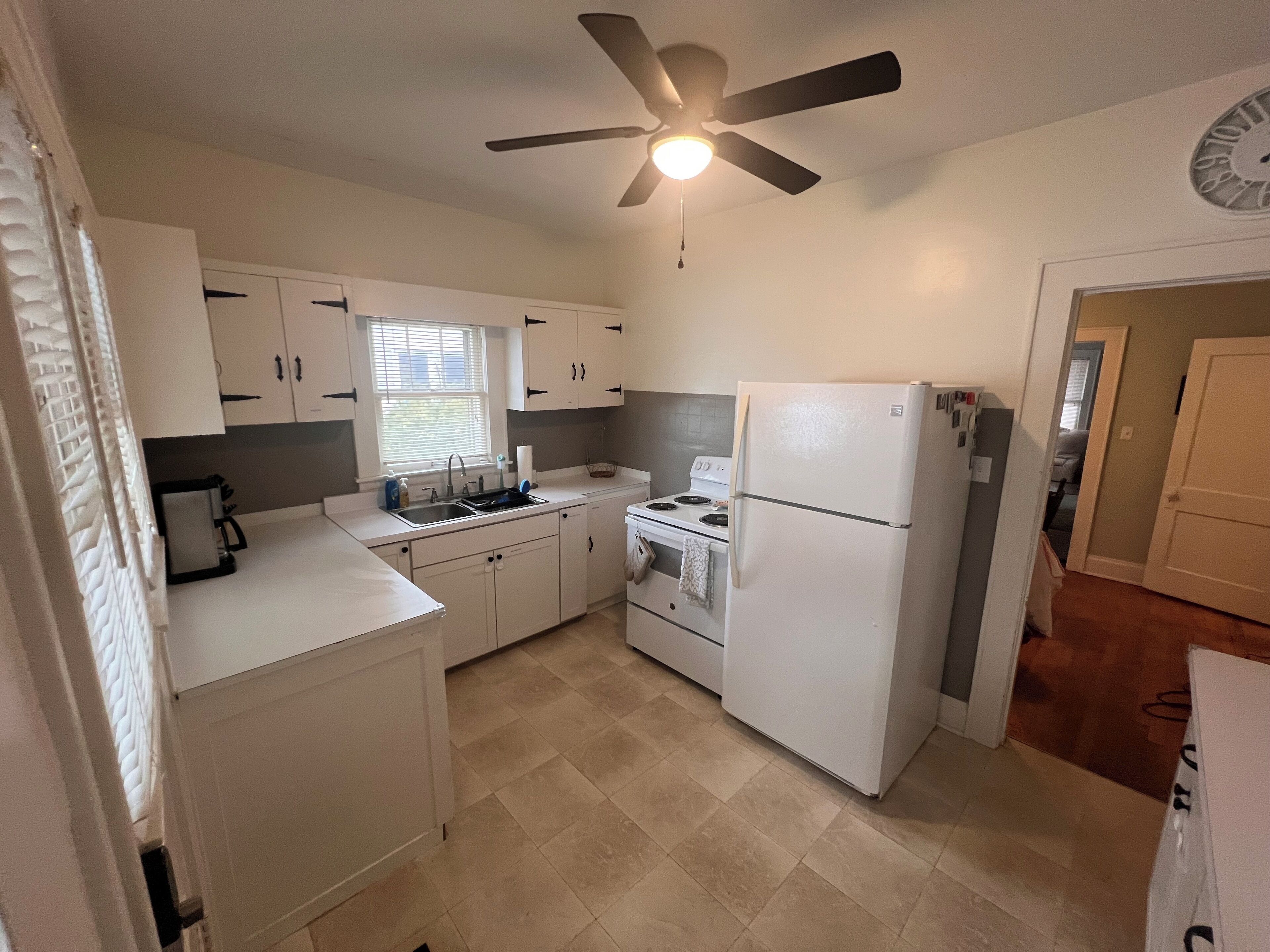 A compact kitchen with white cabinets, a refrigerator, a stove, and a ceiling fan.