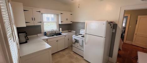 A compact kitchen with white cabinets, a refrigerator, a stove, and a ceiling fan.