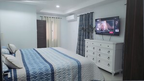 A bedroom with a bed, a dresser, a TV, and a window with curtains.