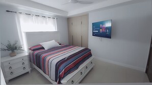 A bedroom with a bed, a TV, a wardrobe, and a window with curtains.