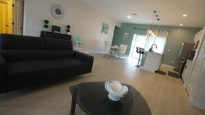 Een moderne woonkamer met een zwarte bank, een glazen salontafel, en een eethoek met een witte tafel en stoelen.