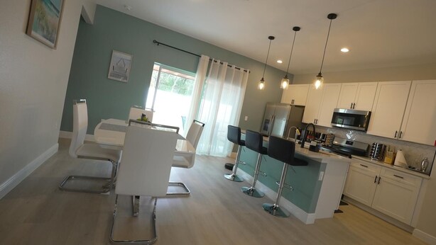Een moderne keuken met witte kasten, een roestvrijstalen koelkast en een magnetron. Er is een eethoek met een witte tafel en stoelen.