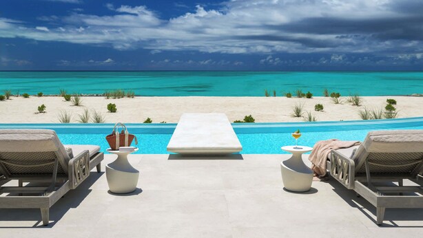 Zona de piscina con sillones de descanso, una mesita y vistas a la playa y al océano.