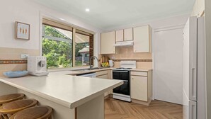 A modern kitchen with a large island, a built-in oven, and a dishwasher. There is a window providing natural light and a view of the outdoors. - 4 Bedrooms, Spacious Backyard, Fireplace, Walk to Beach (Callala Beach)