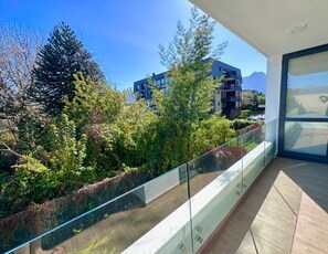 Een balkon met glazen hekwerk, met uitzicht op een tuin en moderne gebouwen.