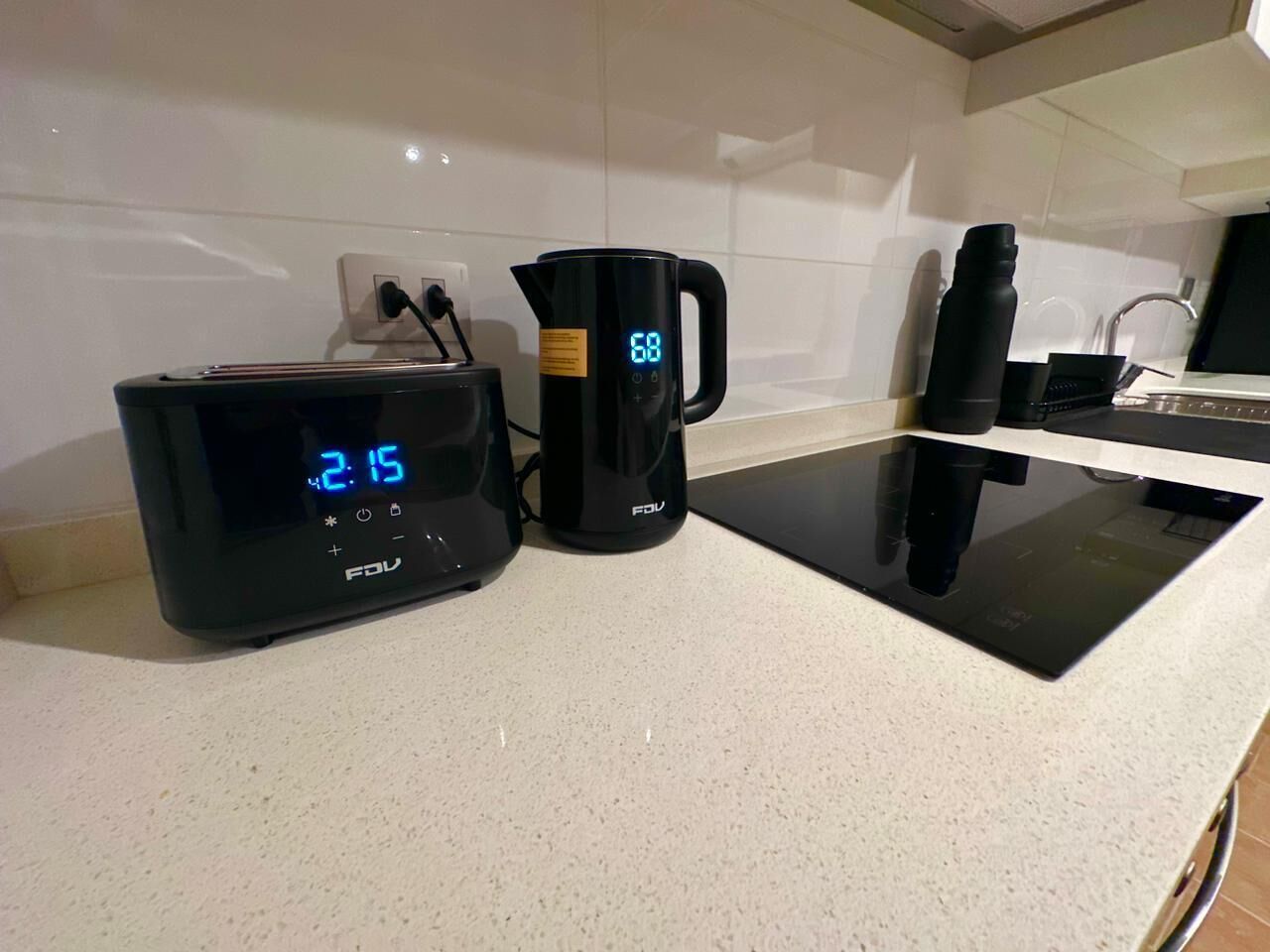 Eine Küchenarbeitsplatte mit einer digitalen Uhr, die 2:15 Uhr anzeigt, einem schwarzen Wasserkocher und einer schwarzen Kaffeemaschine.