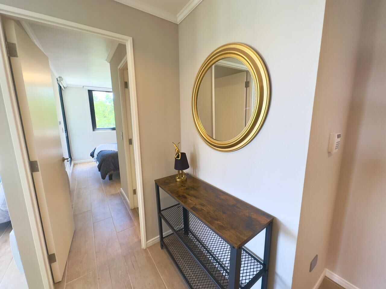 A hallway with a wooden console table, a gold-framed mirror, and a black lamp.