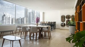 Un moderno comedor con una mesa grande y sillas, vistas a la ciudad a través de amplios ventanales y una planta en maceta.