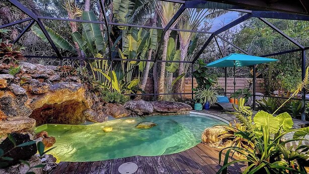 A pool area with a wooden deck, a rock formation, and tropical plants. - Maison Bohème - Adults Only With Pool (Sarasota)