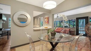 A modern living room with a glass dining table, clear chairs, a round mirror, and a large window with a view of greenery. - Maison Bohème - Adults Only With Pool (Sarasota)