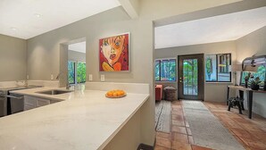 A modern kitchen with a large island, a painting above the island, and a view of the outdoors through the door. - Maison Bohème - Adults Only With Pool (Sarasota)
