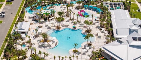 An aerial view of a resort with a central swimming pool, multiple lounge areas, and a parking lot.