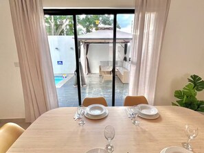Ein Essbereich mit einem Tisch für vier Personen, Blick auf einen Pool und Sitzmöglichkeiten im Freien sowie eine Schiebeglastür zu einem Außenbereich.