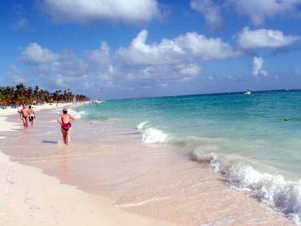 Ein Strand mit klarem türkisblauem Wasser, einem sandigen Ufer und Palmen im Hintergrund.