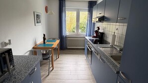 A modern kitchen with blue cabinets, a wooden table, and a window with curtains.