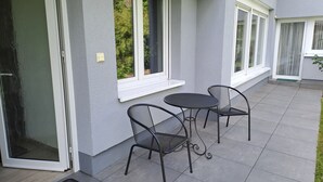 A patio with two metal chairs and a table, a sliding glass door, and a window with a white frame.