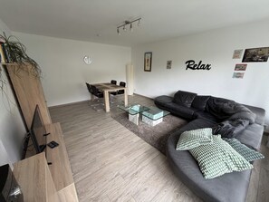 Un salon moderne avec un canapé gris, une table basse en verre, une table à manger en bois avec des chaises et un petit tapis.