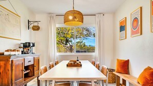 A dining area with a long table, chairs, a bench, a coffee bar, and a large window with a view of trees and mountains. - Boho Escape 3-bedroom house on 1.2 acres minutes from Joshua Tree National Park. (Yucca Valley)