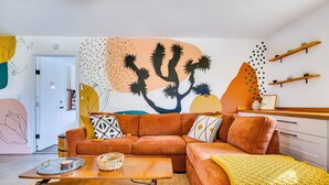A modern living room with a sectional sofa, a coffee table, and a wall mural. - Boho Escape 3-bedroom house on 1.2 acres minutes from Joshua Tree National Park. (Yucca Valley)