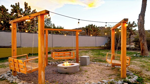 A wooden swing set with a fire pit in the center, surrounded by rocks and a grassy area. - Boho Escape 3-bedroom house on 1.2 acres minutes from Joshua Tree National Park. (Yucca Valley)