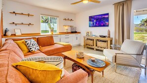A modern living room with a sofa, armchairs, a coffee table, and a dining area. There is a ceiling fan, a painting on the wall, and a window with a view of the outdoors. - Boho Escape 3-bedroom house on 1.2 acres minutes from Joshua Tree National Park. (Yucca Valley)