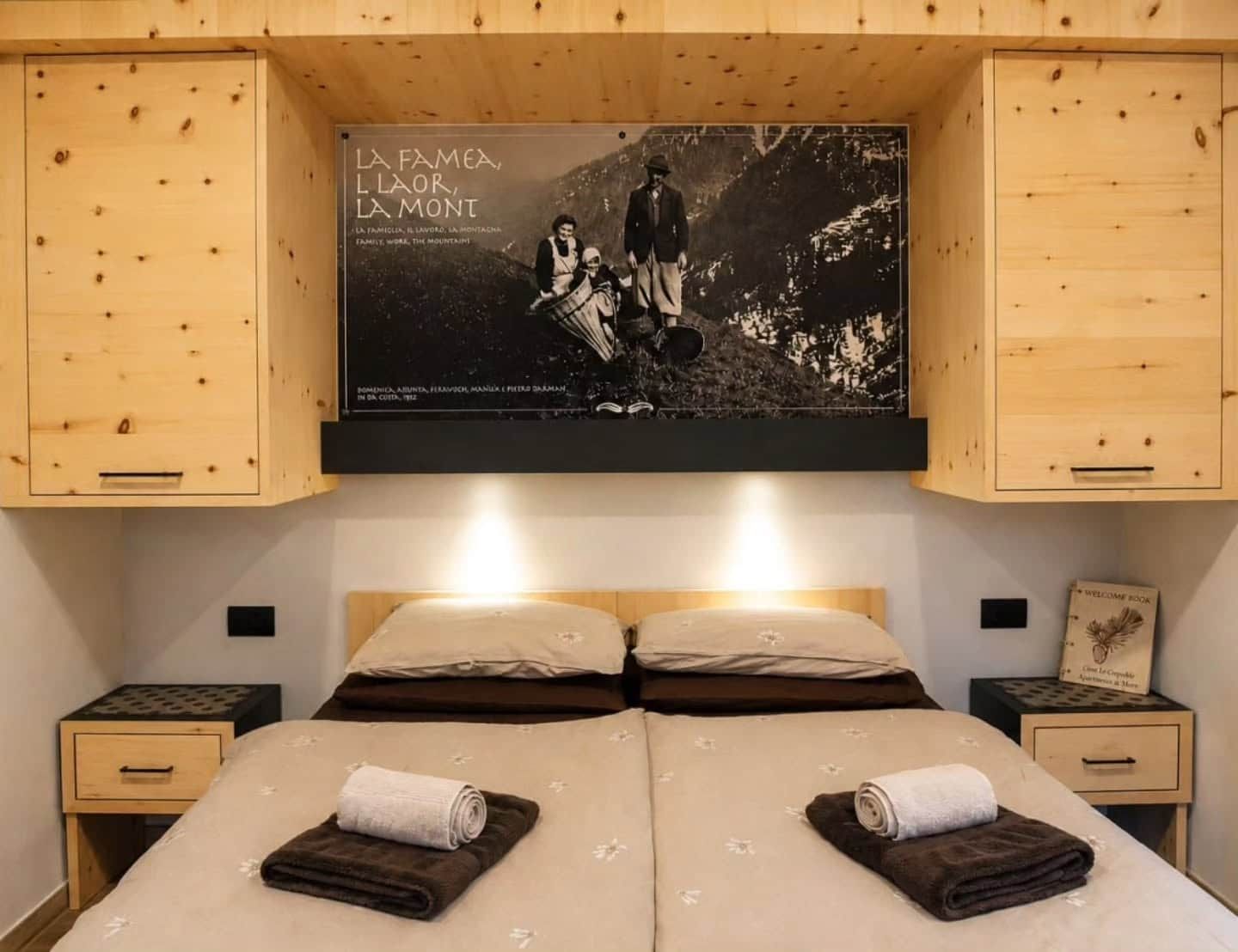 Een hotelkamer met een bed, twee nachtkastjes en een aan de muur bevestigde televisie waarop een foto van een gezin staat.