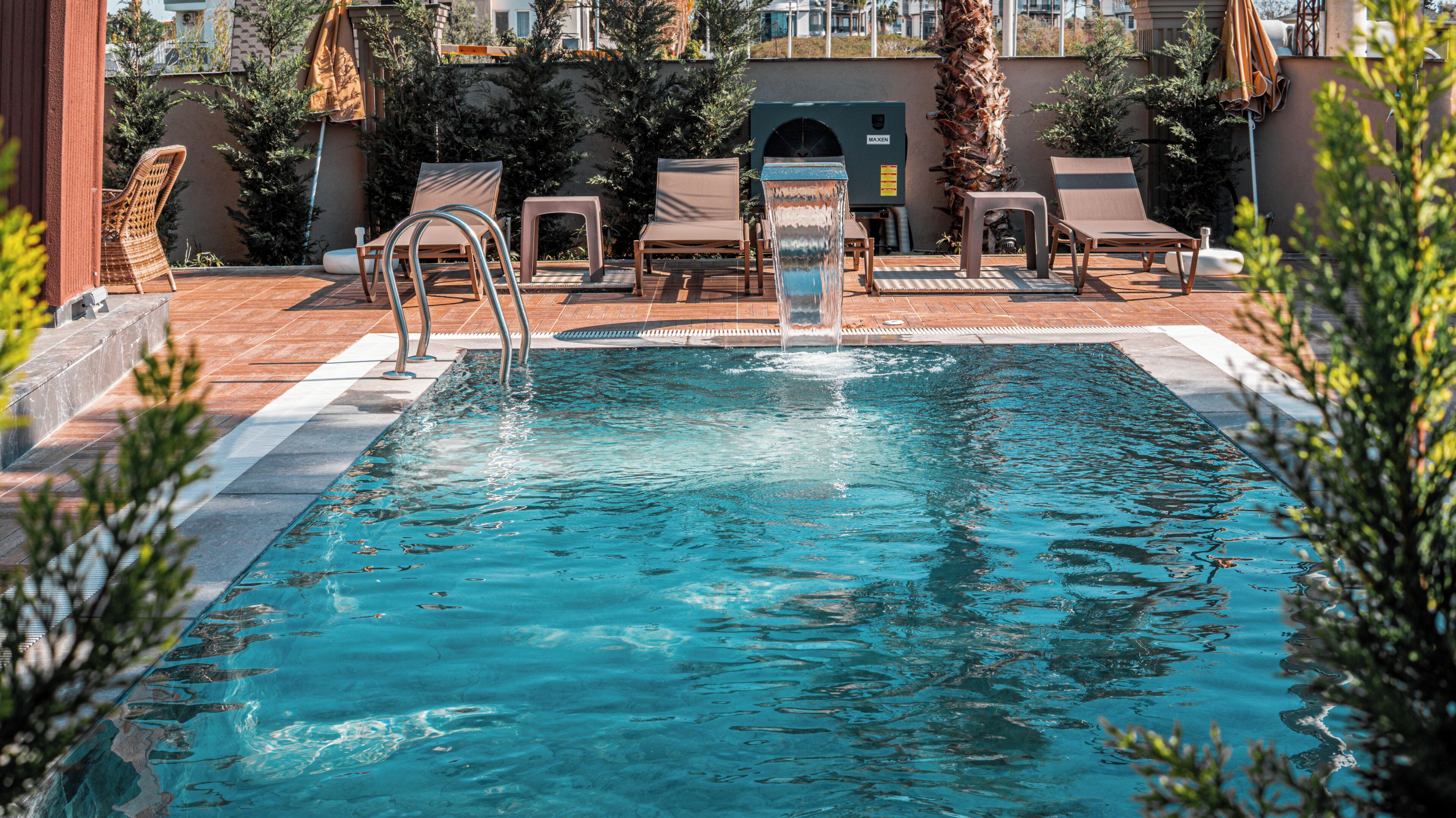Piscina com espreguiçadeiras, um elemento aquático e um edifício ao fundo.