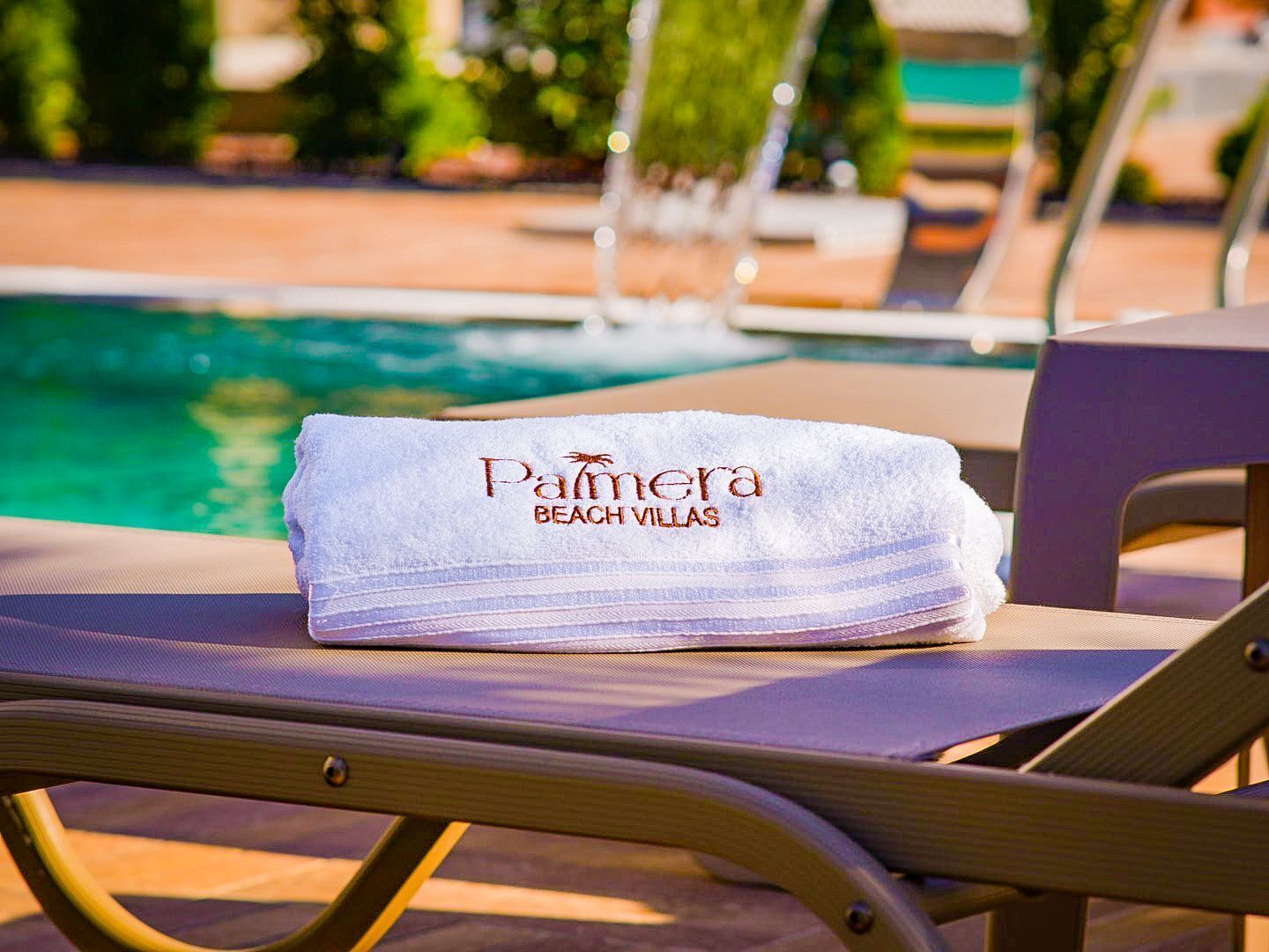 Una toalla con el bordado 'Panamera Beach Villas', sobre una silla de descanso junto a una piscina.