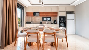 A modern kitchen with a dining area, featuring a large island, wooden cabinets, and a built-in oven. - Palmera Beach Villas (Alanya)