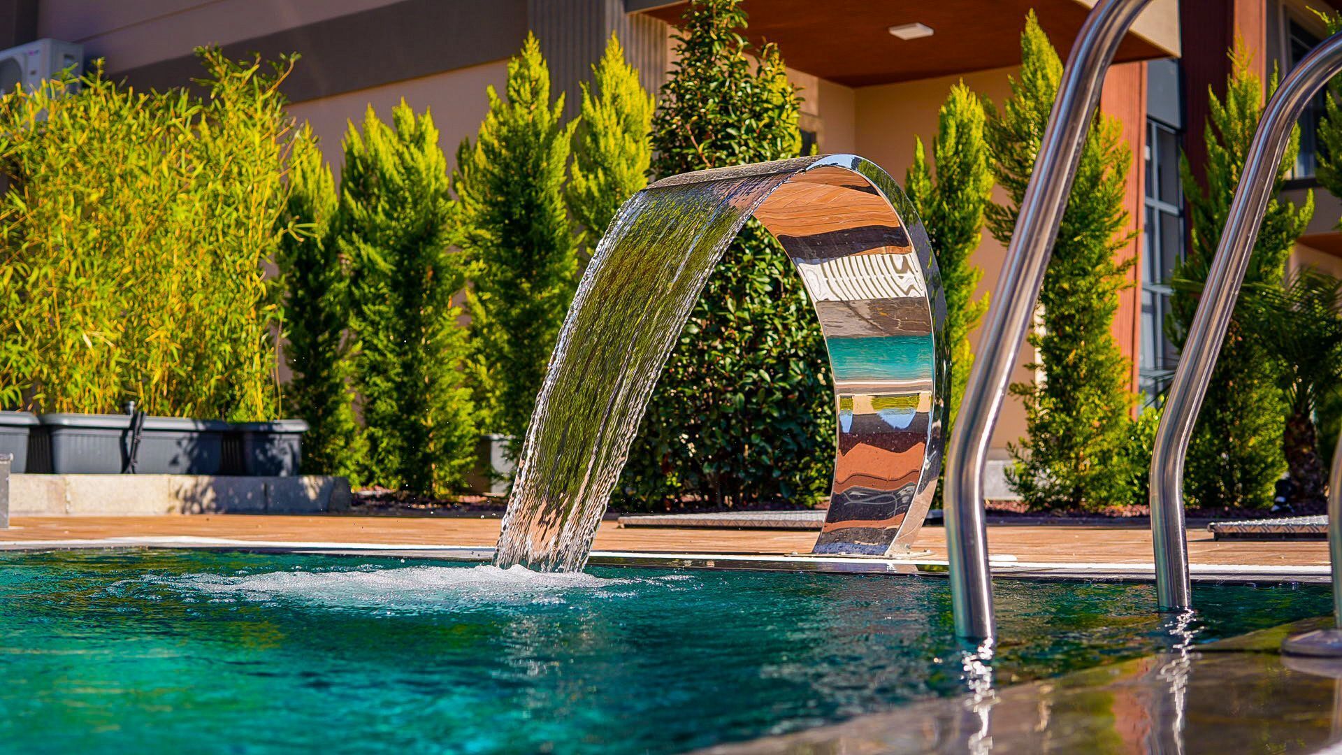 Una piscina con una cascata, circondata da vegetazione e un edificio moderno.