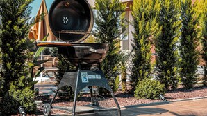 A portable barbecue grill with a metal grate, a lid, and a handle, set up outdoors with trees and a building in the background. - Palmera Beach Villas (Alanya)