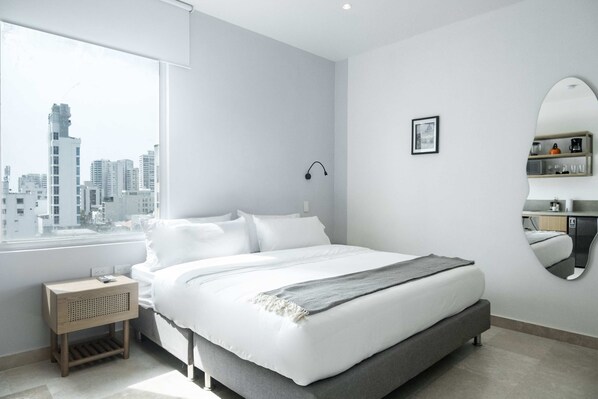 A modern bedroom with a large bed, a bedside table, a mirror, and a view of the cityscape. - w* | Exclusive Loft in the Heart of Bocagrande (Cartagena de Indias)