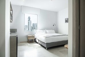 A modern bedroom with a large window, a bed, a bedside table, and a small wooden stool. - w* | Exclusive Loft in the Heart of Bocagrande (Cartagena de Indias)