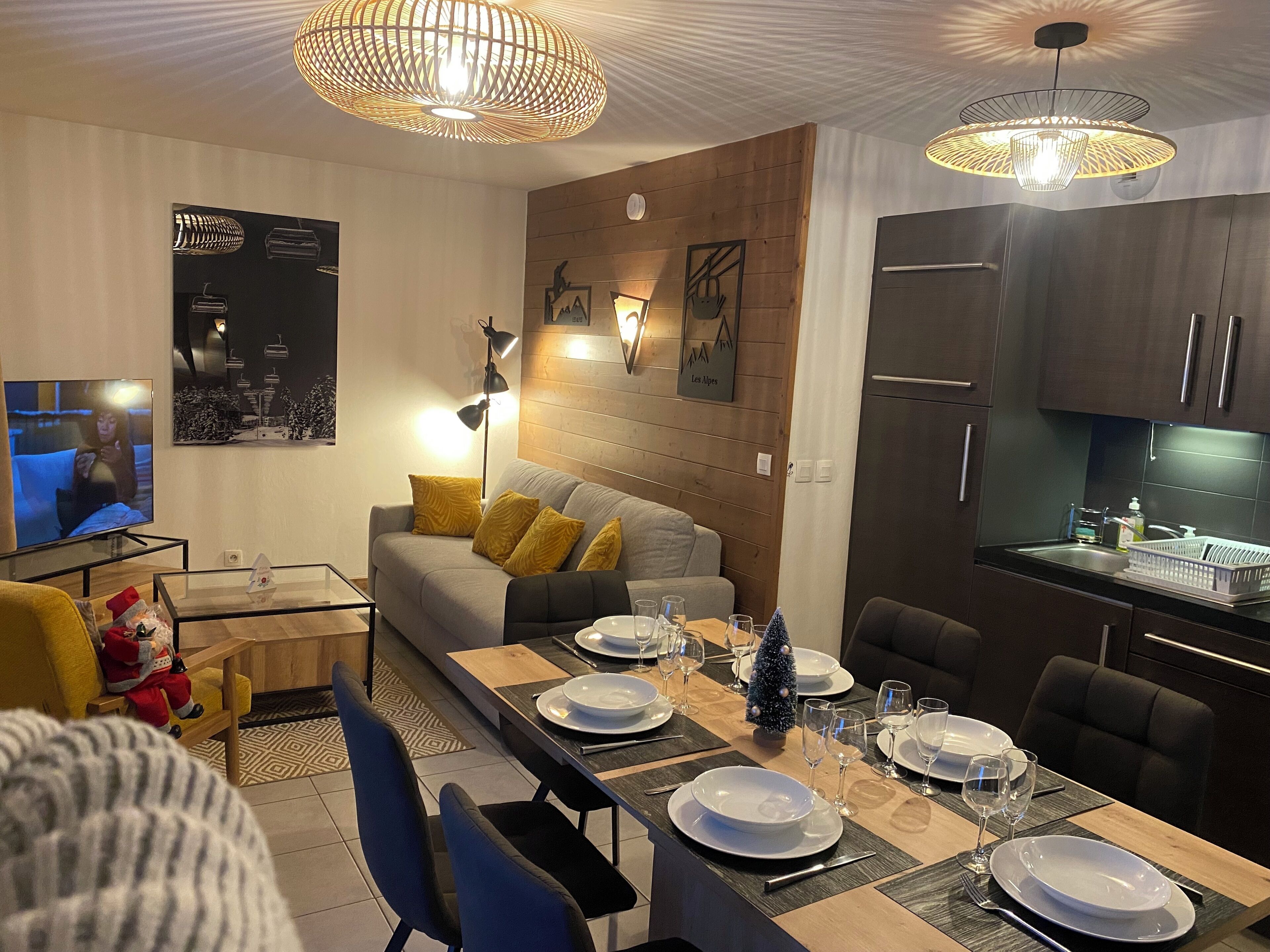 Una sala moderna con un sofá, una mesa de comedor preparada para cuatro personas y una cocina con armarios oscuros y un refrigerador.