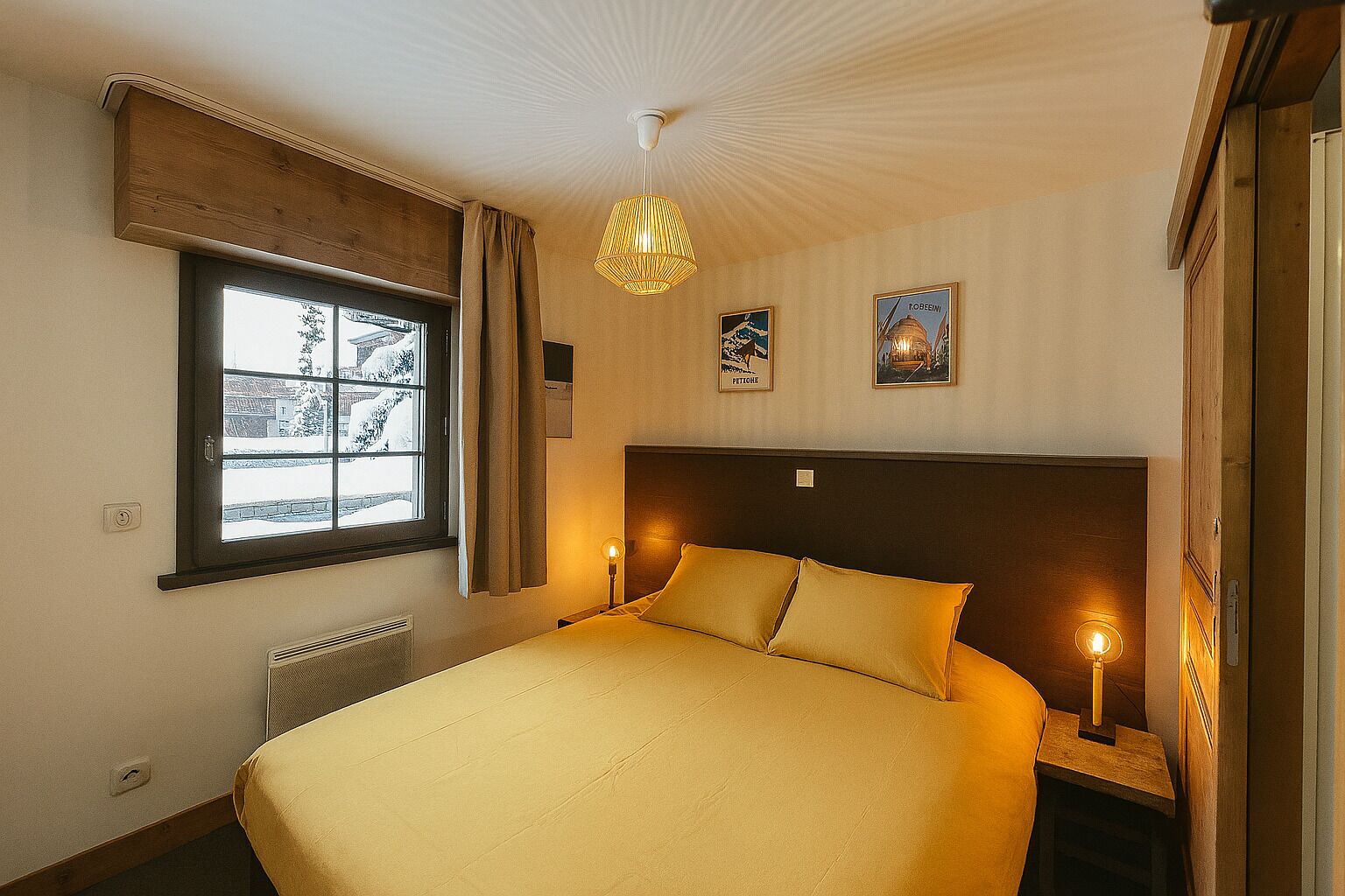 Et hotelværelse med en stor seng, et vindue med udsigt over et snelandskab, en hængende lampe og to vægmonterede lamper.