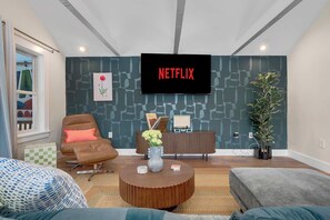 Un salon moderne avec un téléviseur à écran plat fixé au mur, un fauteuil en cuir marron, une table basse ronde ornée d’un vase et un canapé gris.