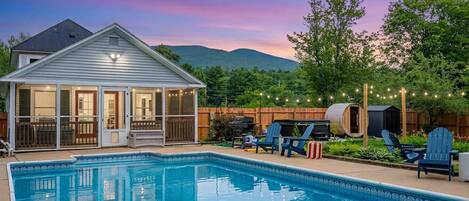 A swimming pool with a covered patio, deck chairs, and a barbecue area.