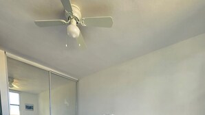 Ein Hotelzimmer mit zwei Betten, einem Deckenventilator, einem großen Spiegel und einer Lampe.