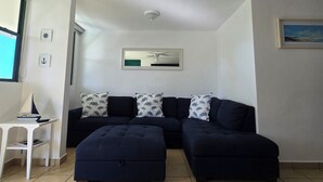 Ein Wohnzimmer mit Ecksofa, Deckenventilator und einem kleinen weißen Tisch mit einem Modellschiff.