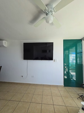 A room with a ceiling fan, a mounted TV, and a green door. - Beach-5 Pools-25 Min from airport-Unit with reserve water system  (Loíza)