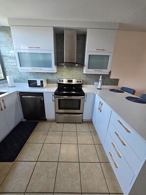 A modern kitchen with white cabinets, stainless steel appliances, and a tiled floor. - Beach-5 Pools-25 Min from airport-Unit with reserve water system  (Loíza)