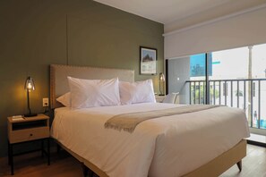 A neatly made bed with a headboard, a bedside table with a lamp, and a window with a view of buildings. - w* | Shining 1BR w/ Perfect Balcony in Miraflores (Miraflores)