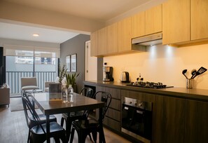 A modern kitchen with wooden cabinets, a gas stove, and a coffee maker. There is a dining area with a table and chairs. - w* | Prime 2BR w/ Balcony in Miraflores (Miraflores)