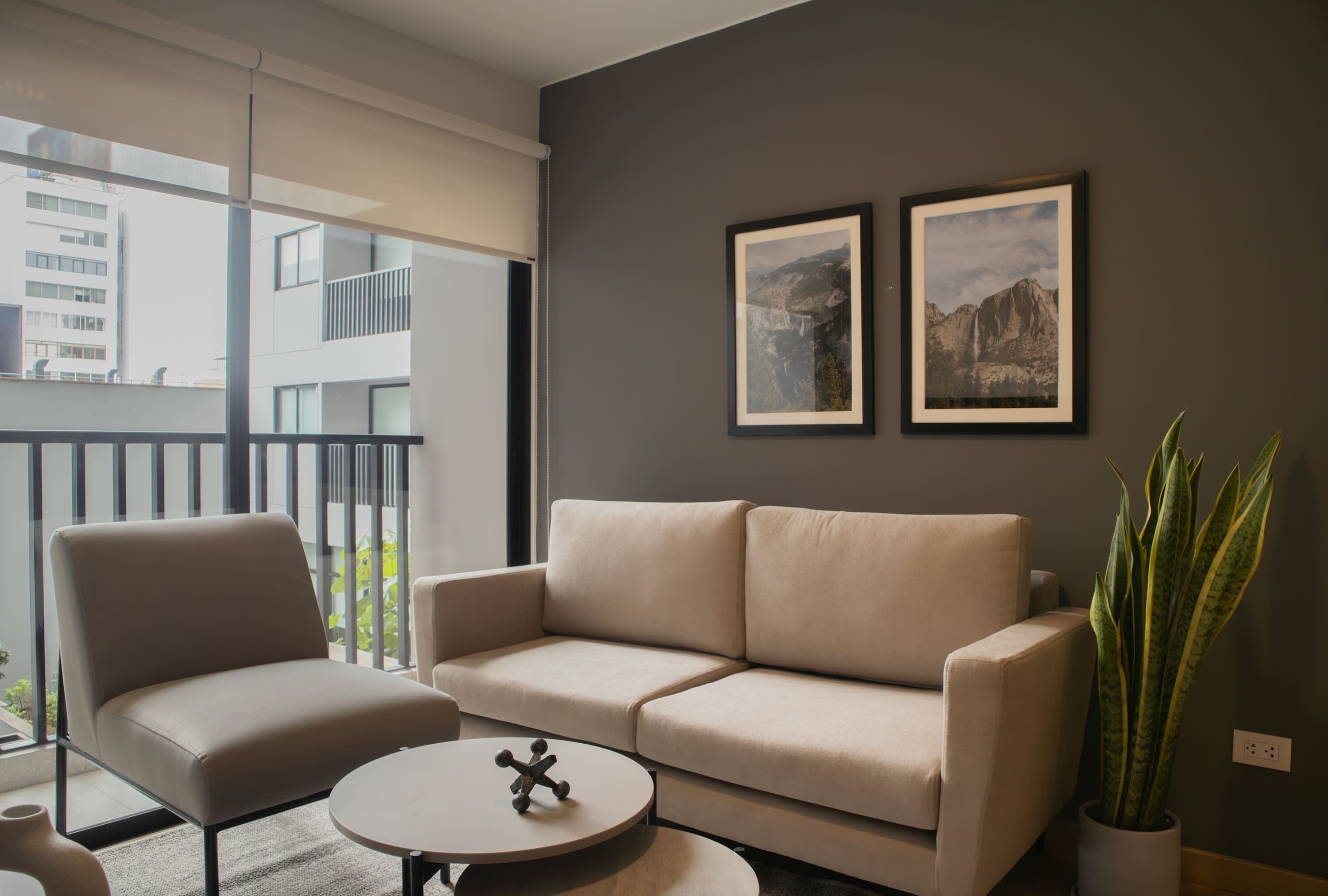 Una sala de estar moderna con un sofá color beige, una mesa de centro redonda y una planta en maceta.