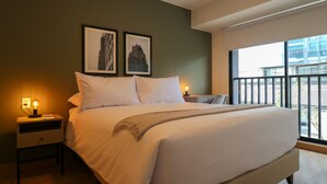 Una camera da letto moderna con un letto grande, due comodini, un tavolino e una finestra con vista sugli edifici.