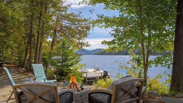 A lakeside deck with outdoor seating, a fire pit, and a dock extending into the water. - Pondside Cottage w/ Dock & Patio! [Loons Nest] (Mount Desert)