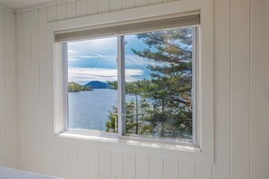 A window with a view of a lake and trees. - Pondside Cottage w/ Dock & Patio! [Loons Nest] (Mount Desert)
