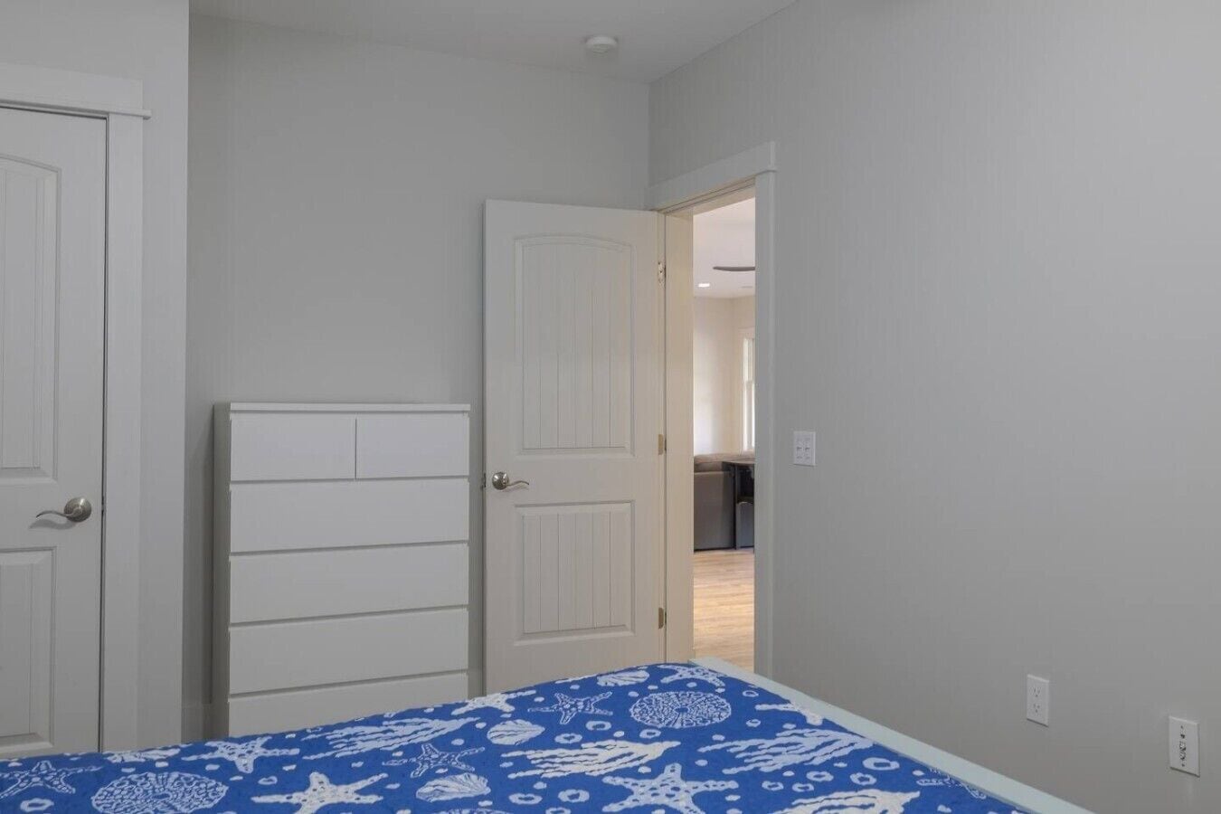 A bedroom with a bed, two doors, and a hallway leading to a kitchen area.